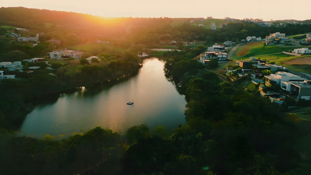 Lago do condomínio ao pôr do sol, cercado por casas e mata