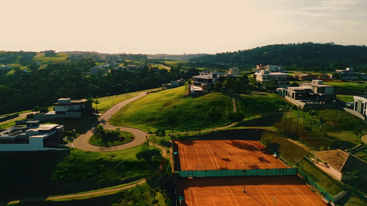 Quadras de tênis de saibro vistas do alto, entre as casas e a mata do condomínio
